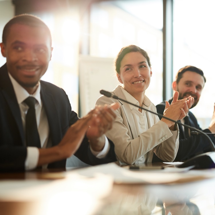A group of diverse professionals smiling and applauding during a meeting.