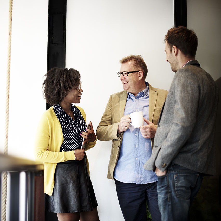 A group of three professionals engaging in a friendly conversation, showcasing a diverse workplace atmosphere.