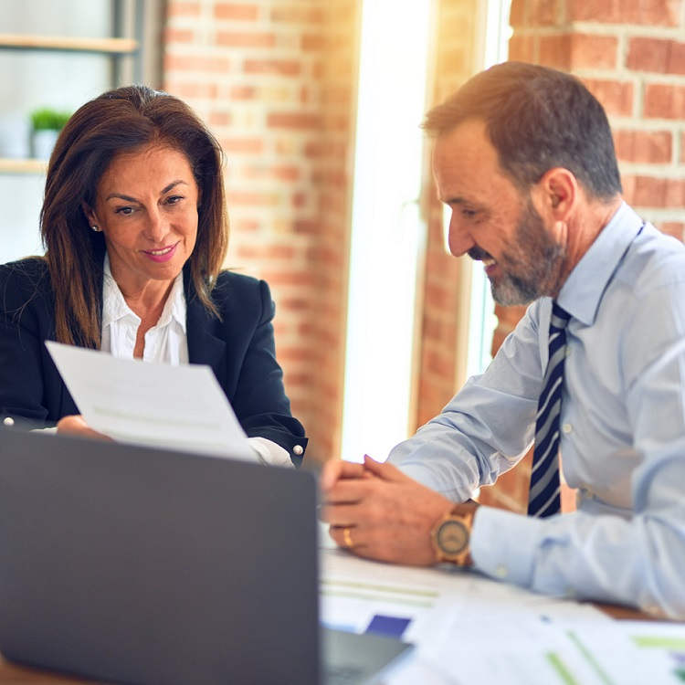 A professional woman and man collaborate over documents in a well-lit office setting.
