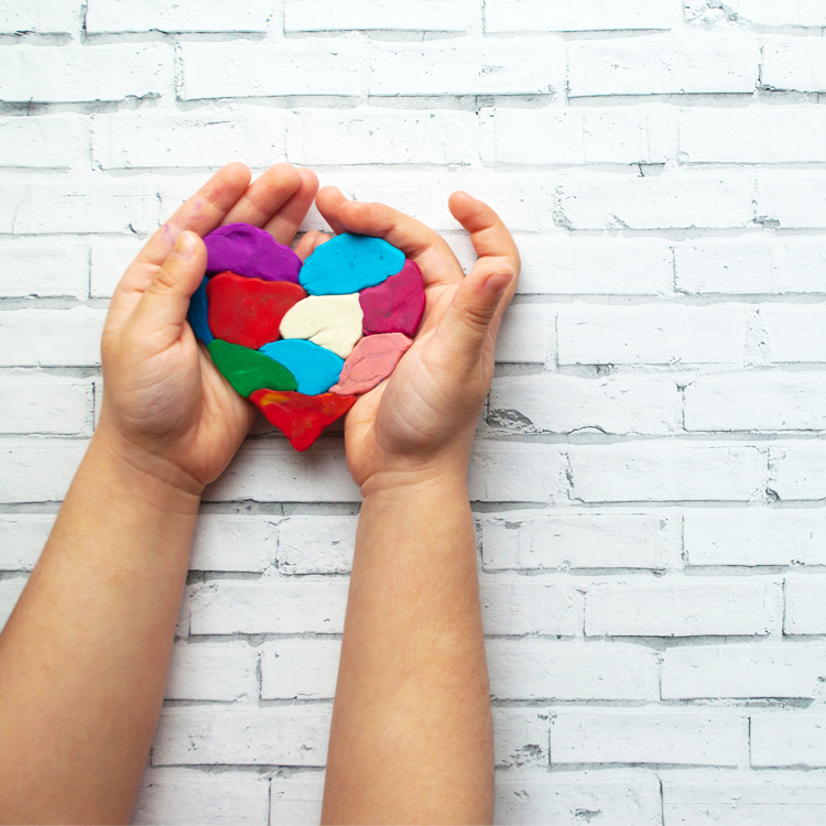 hands holding a heart made of multi-color clay pieces