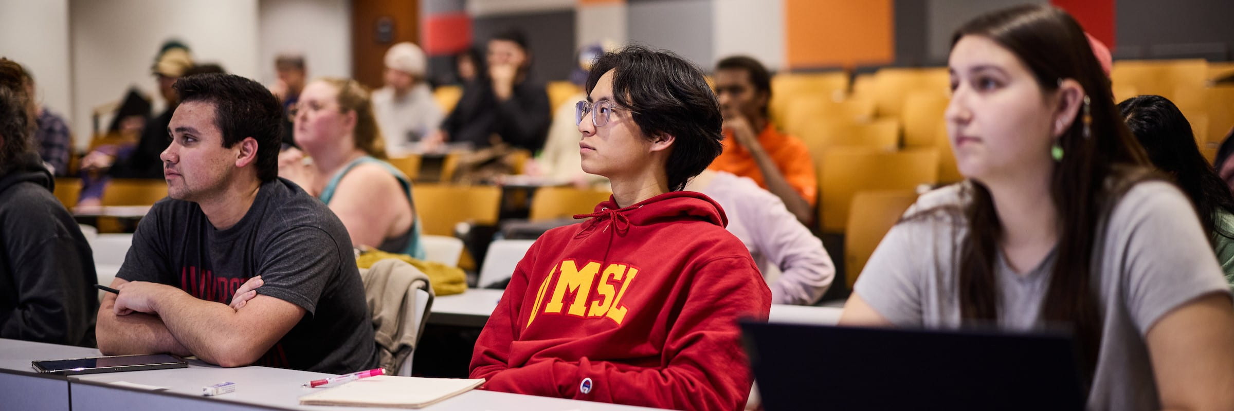 Several students work listen to a lecture in a lecture hall