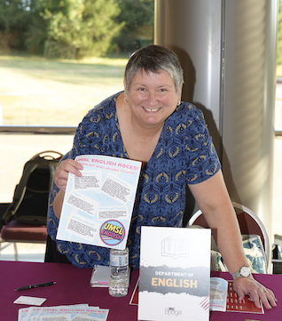Dr. Lynn Staley, smiling and holding an English Department flyer