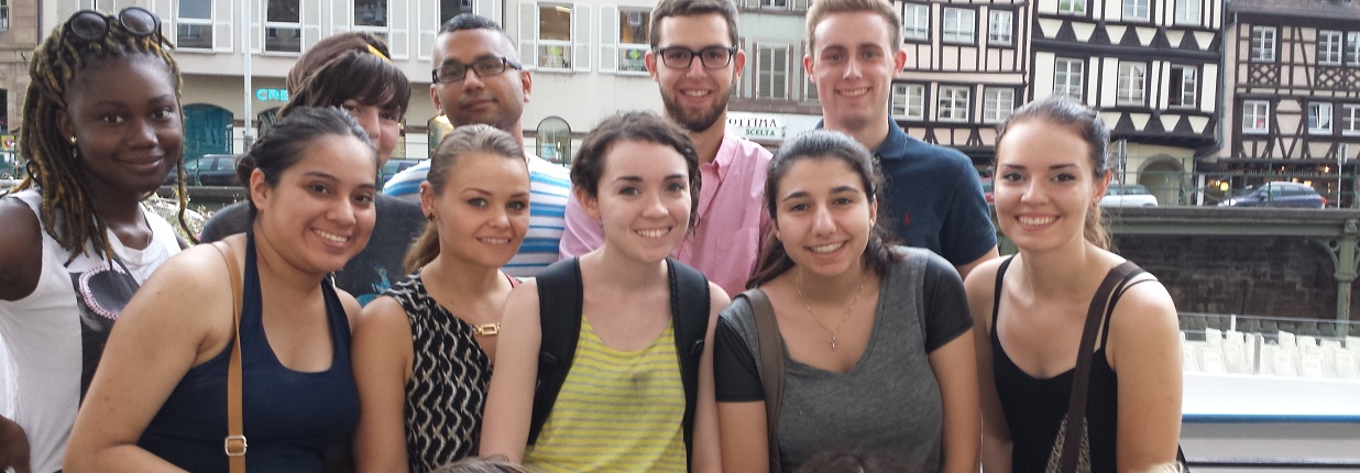 Ten people, five in front in a line and five in back in a line, smile at the camera in a setting background of a European nation