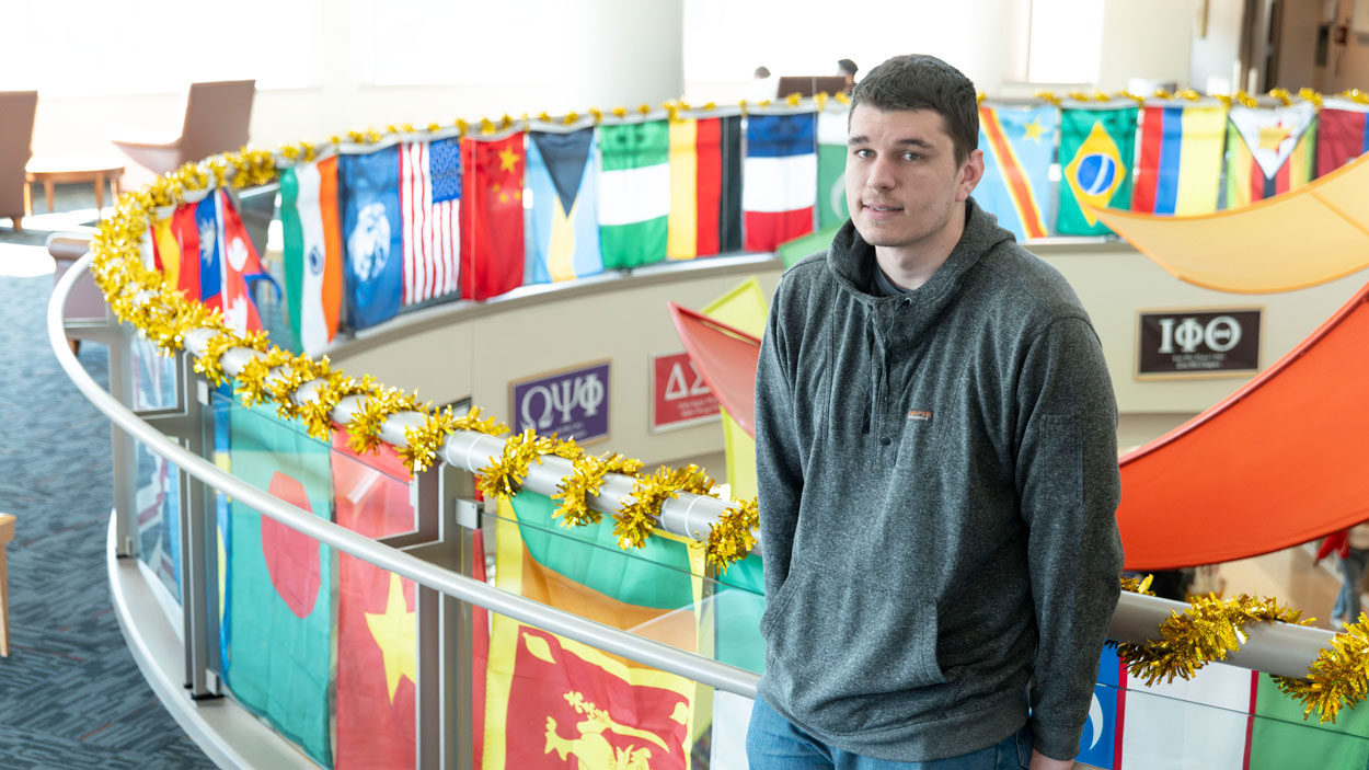Jon Velier stands in front of MSC balcony rail surrounded by flags, smiling at the camera