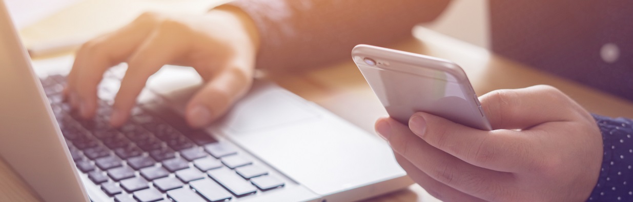 Person with a phone in hand working on a laptop