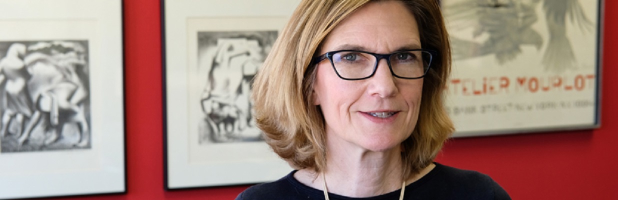 white woman with blonde hair and glasses stands in front of framed artwork