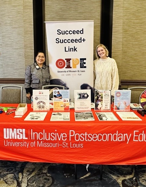 Two women by the red table of the Office of Inclusive Postsecondary Ed