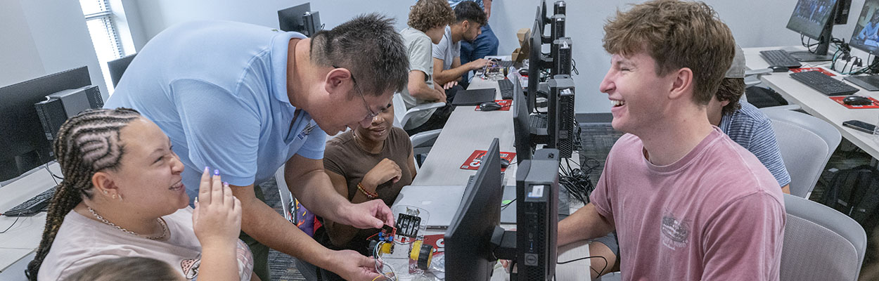 two engineering students laughing while other students are working with a professor