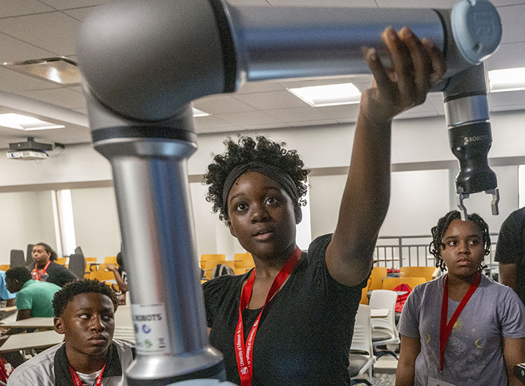 A camper interacts with a robotic arm during an UMSL Engineering Camp.