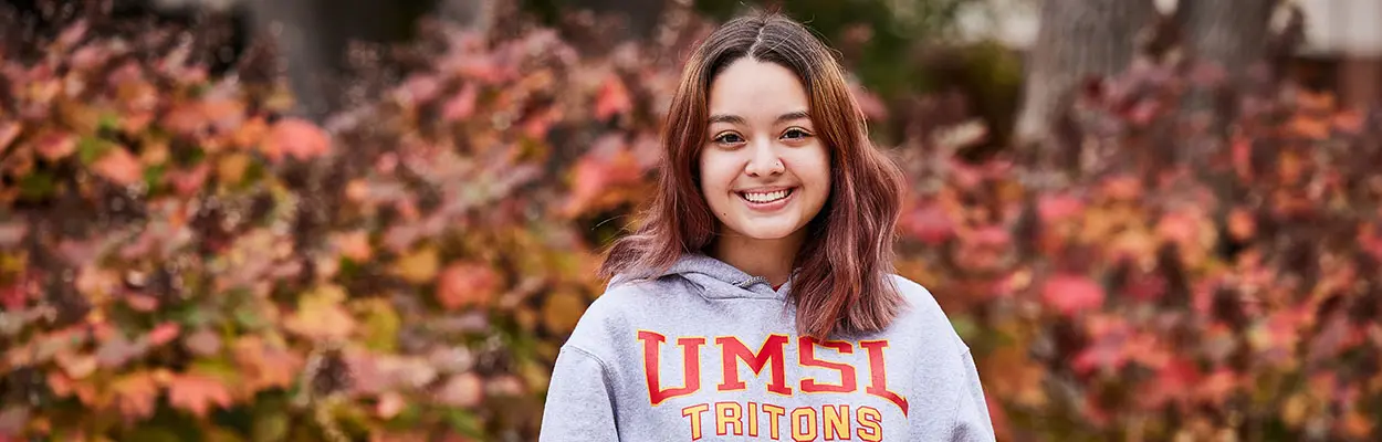 UMSL student in an UMSL hoodie in front of fall scenery