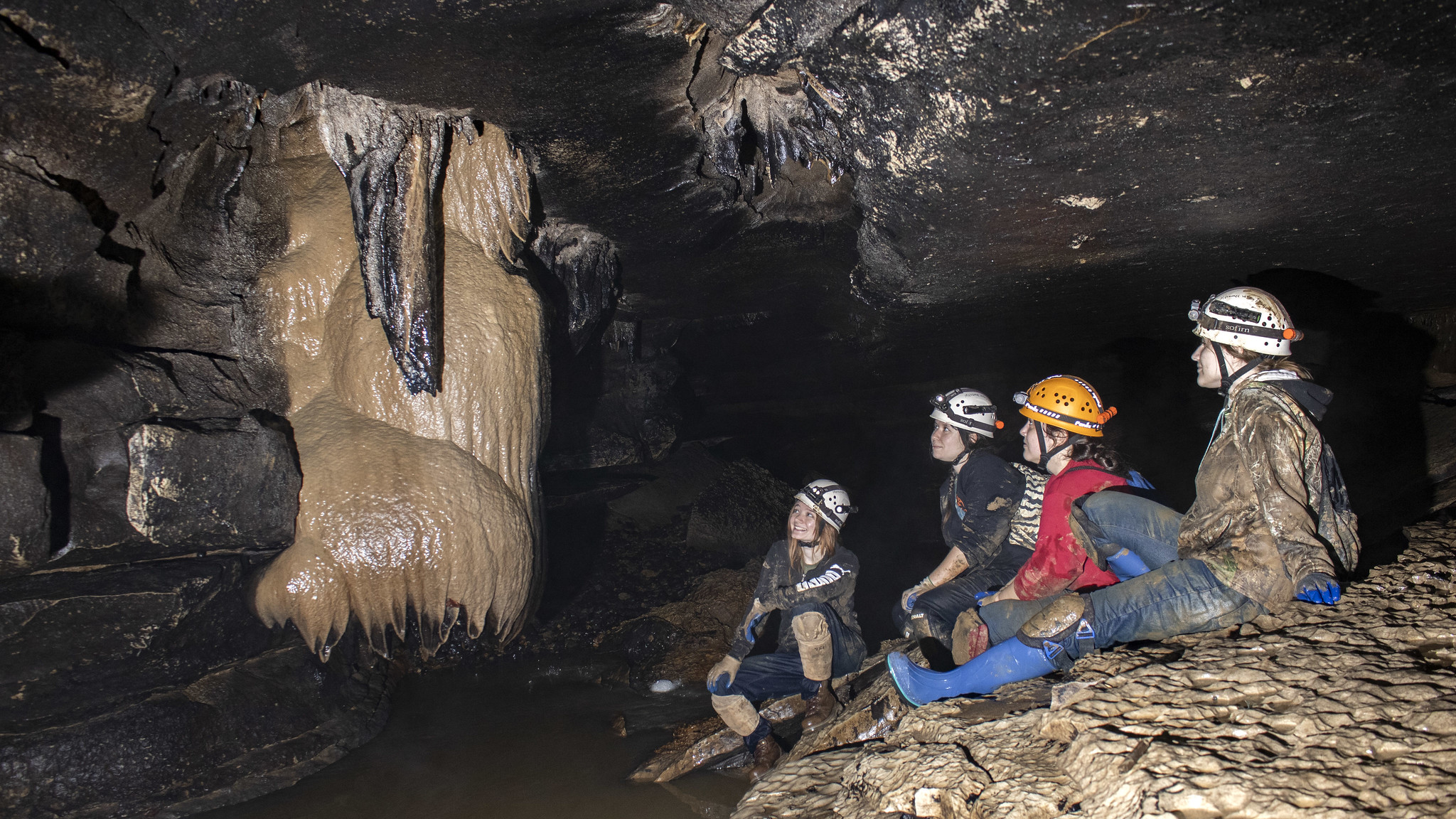 A focused picture of EAO members covered in mud admiring the structure of the cave with a flash showing their awe.