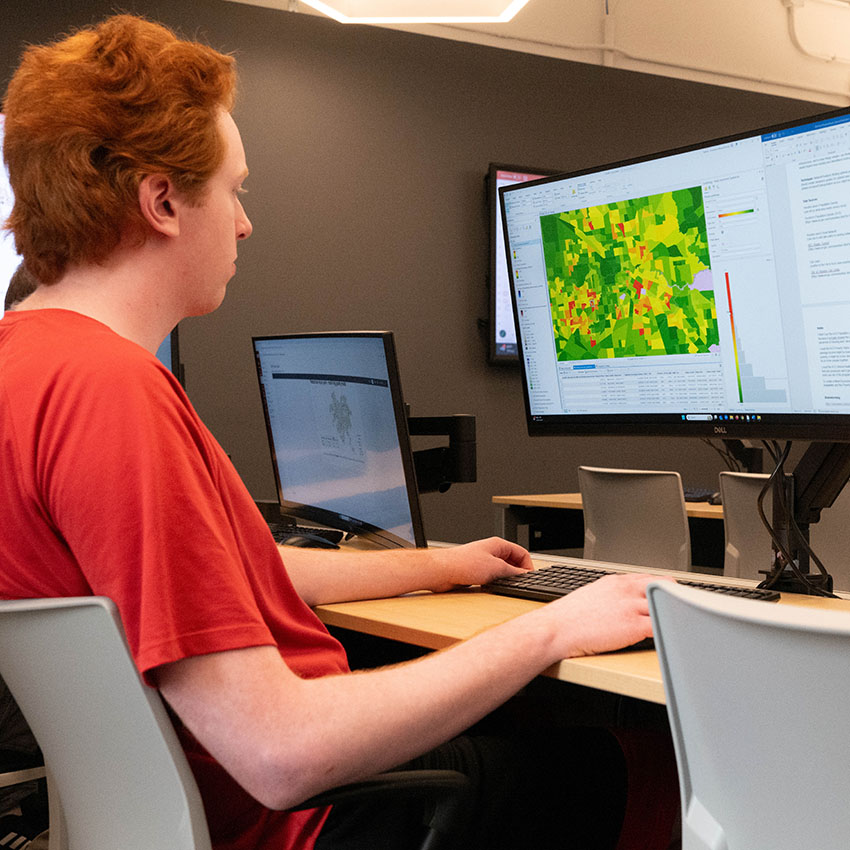 UMSL Student sitting in a computer lab classroom looking at a map