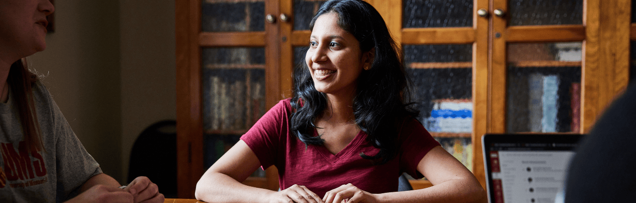 student in a red UMSL shirt sitting at a table in conversation