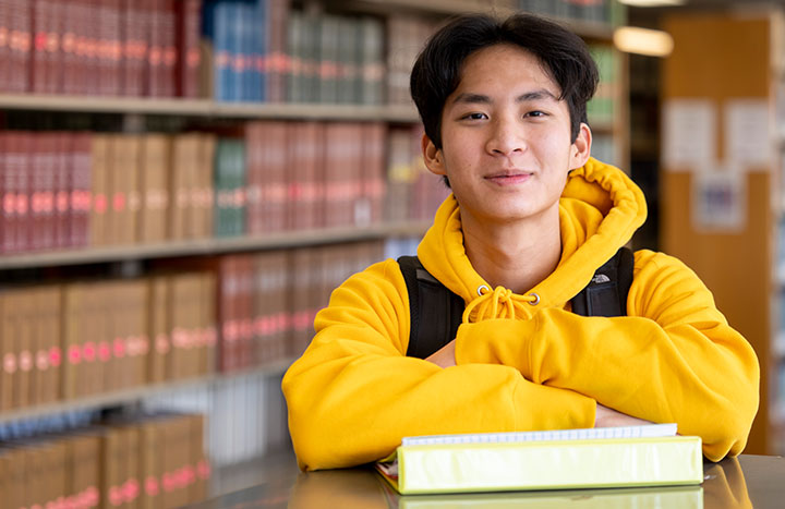 Seated student with arms resting on binders at a table.