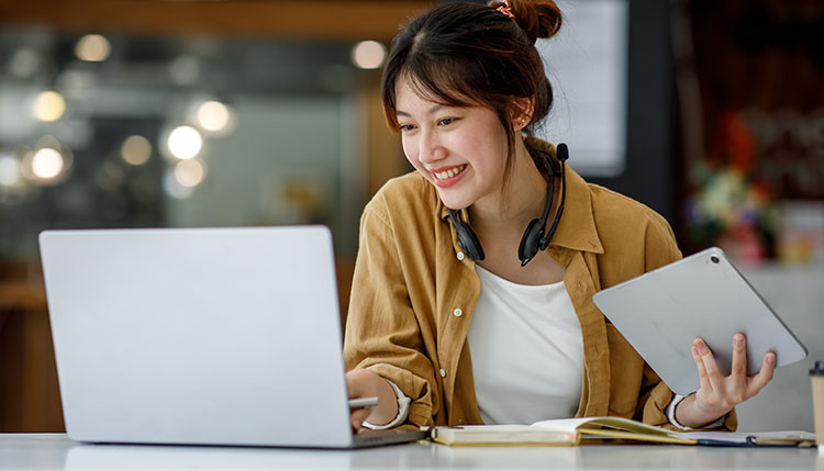 student working on a laptop with a tablet in hand