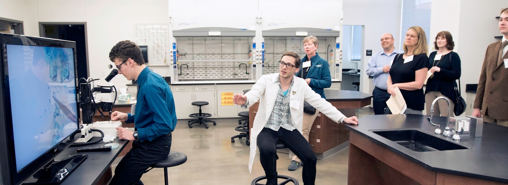 professor and student explaining an experiment to visitors in a lab