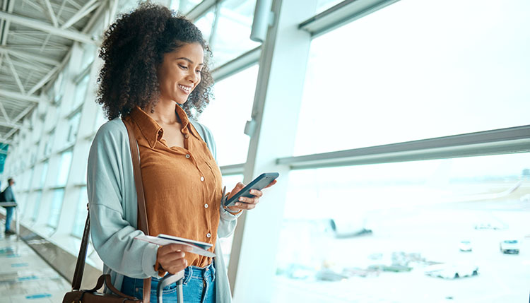 woman standing by an airport window with boarding pass and suitcase