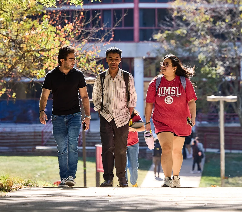 Long shot of three students walking along pathway in conversation