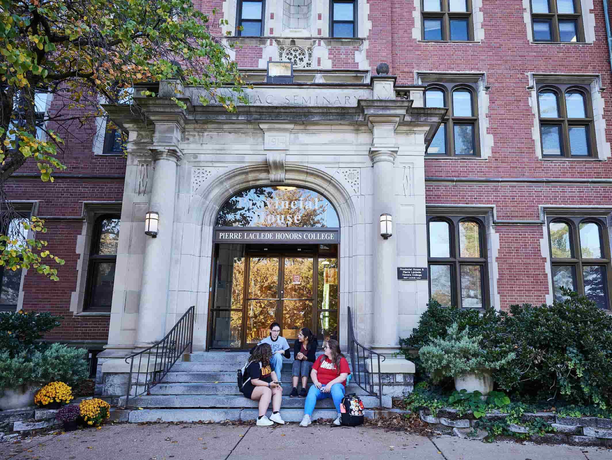 Four students converse on the front steps of the Pierre Laclede Honors College
