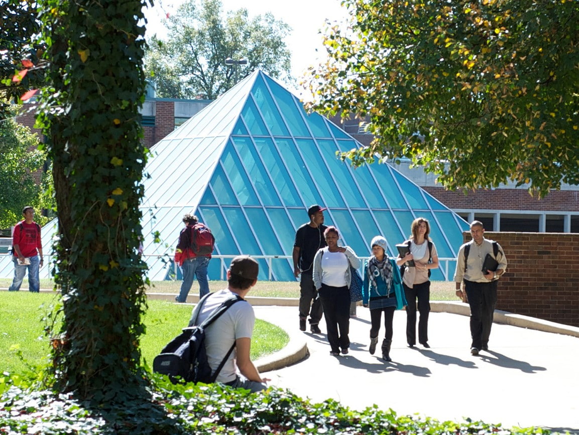 A group of students walking outside in front of the glass pyramid of the Mercantile Library