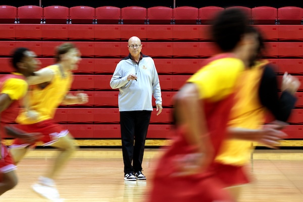 A basketball coach observes players during practice in a gymnasium.