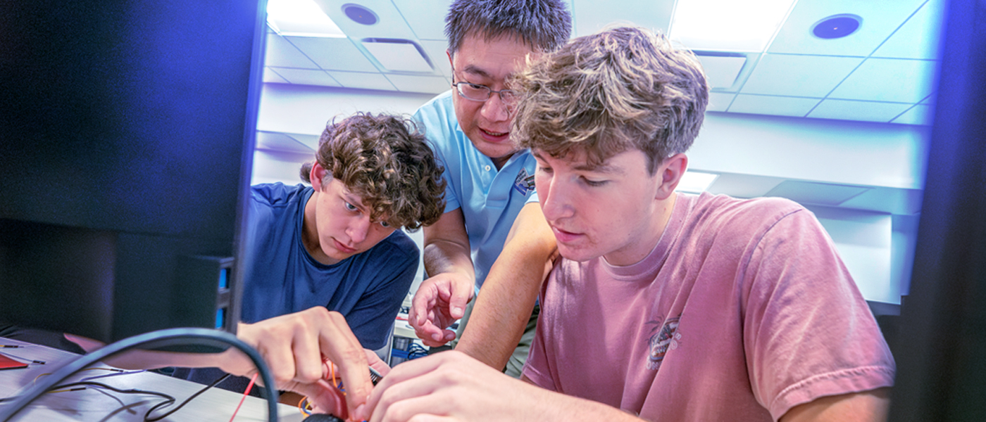 Students collaborating on a project with an instructor, focusing on electronics and hands-on learning.