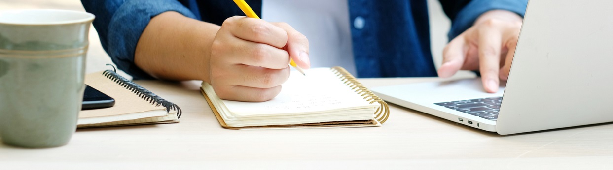 Image of a man with a notebook paper, pen and alaptop