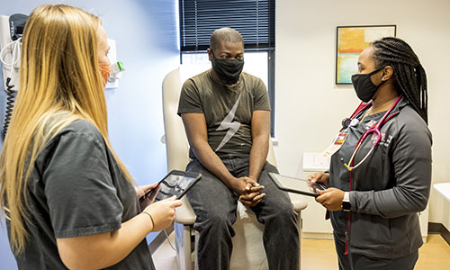 Two student nurses talking to a patient on a exam bed