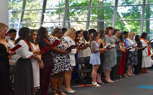 graduates stand in a line indoors, during a ceremony.