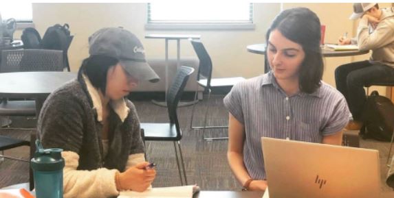 Two students sit at a table in the UMSL tutoring center and discuss a paper.