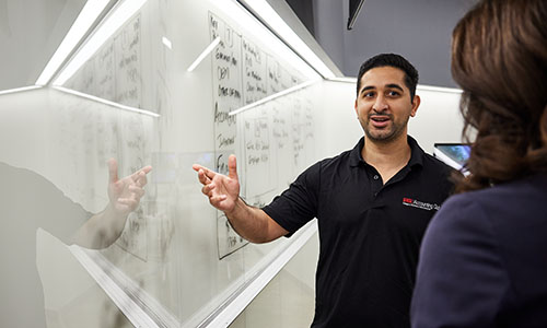 student speaking with a professor while pointing at a white board