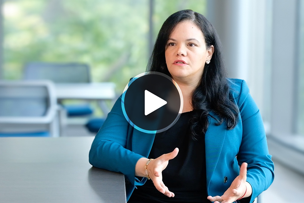 Woman in a blue blazer speaking and gesturing while seated at a conference table.