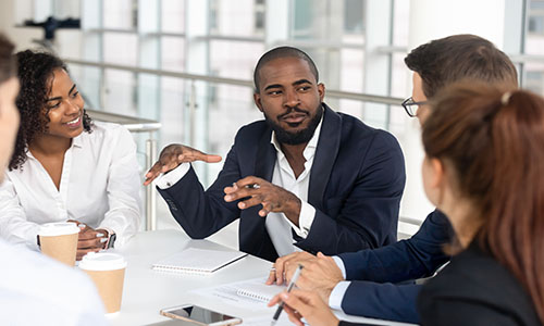 Man leading a meeting of people sitting at a table