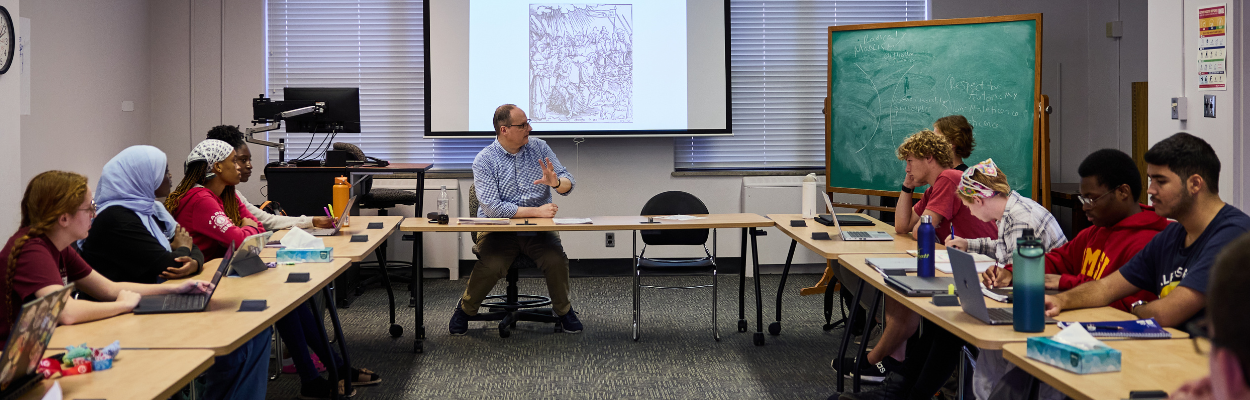 seated professor speaking to class