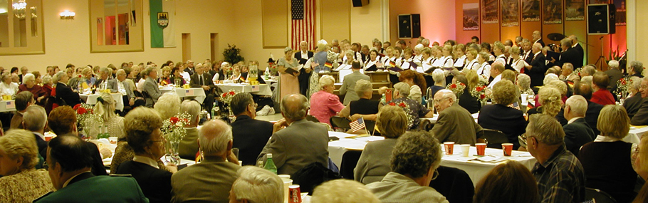 Large group of people at a dinner event watching a choir performance 