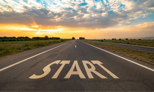 Early morning view of an empty road stretching ahead through a flat landscape. The word START is painted on the road.