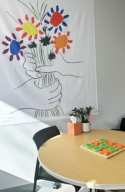 an office with a sketch of a bouquet of flowers above a table with 2 chairs and a checkers set