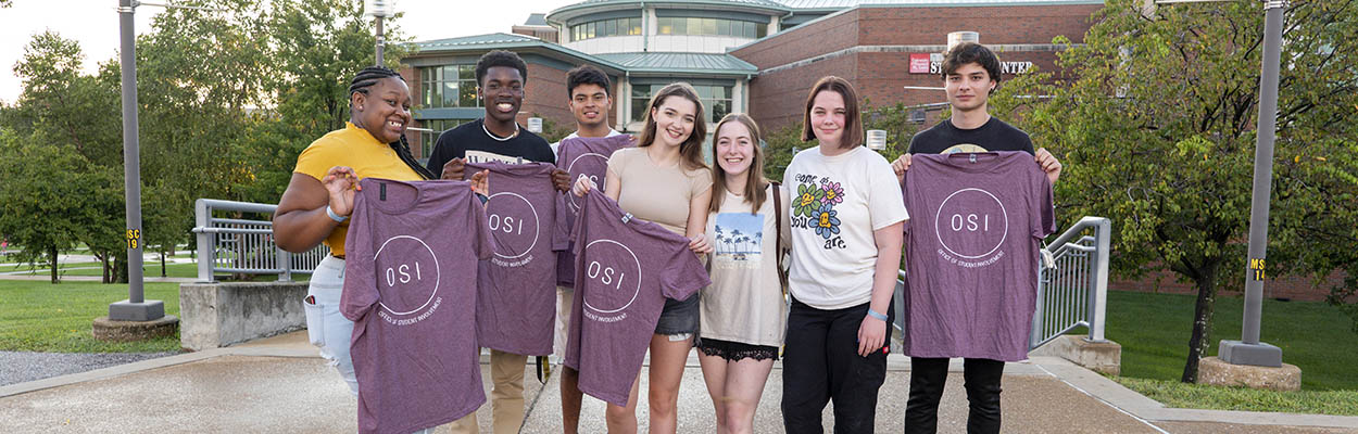 A group of students attending the Welcome Back Bash, a signature UMSL event in the Fall. The students are holding up t-shirts from the Office of Student Involvement. 