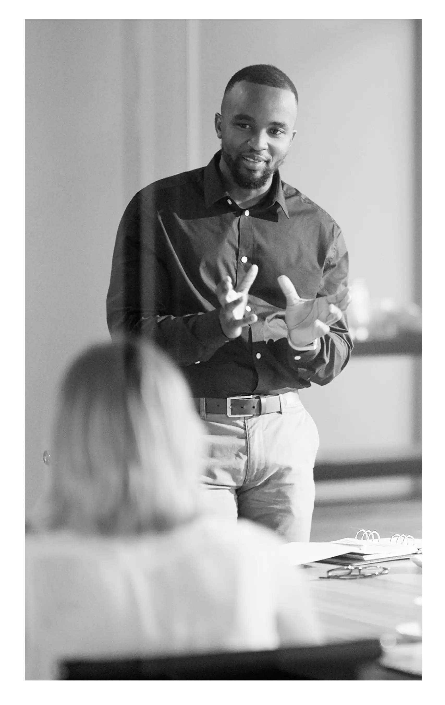 A professional man in a blue shirt presents ideas to a small group in a modern meeting room.