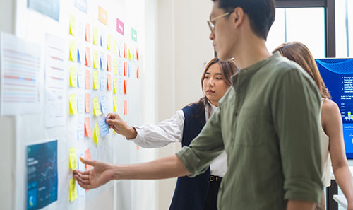 three people reading and reaching for post it notes on a white wall