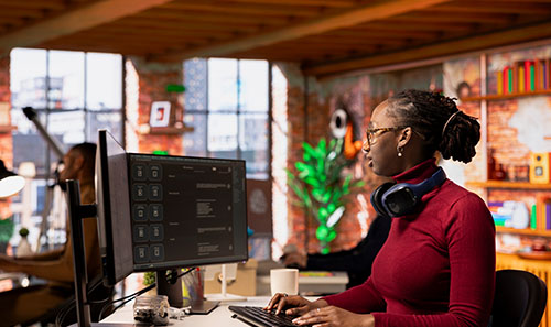 A woman sits at a desk with a computer. The computer screen has an artificial intelligence application on screen.