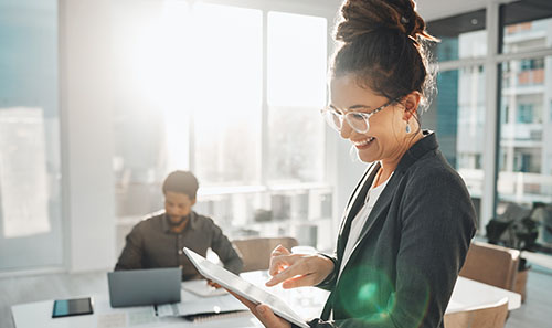 A woman stands in an office holding a tablet working with business software.