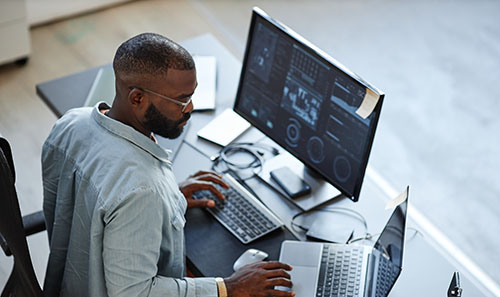 Overhead view of a man working with his computer. On his computer screen are excel charts, and data modeling tools.