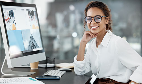 a woman smiling at the camera in front of a larger computer monitor
