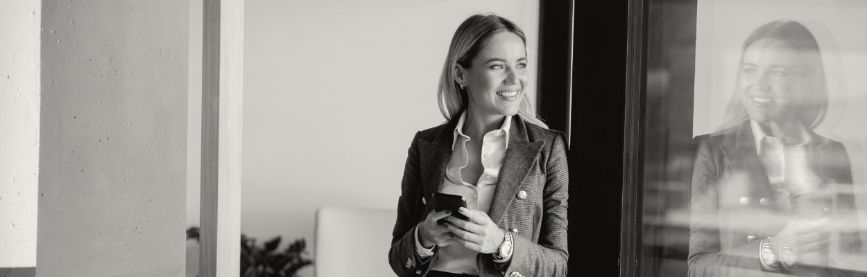 Businesswoman reading messages on smartphone in modern office, daytime reflection