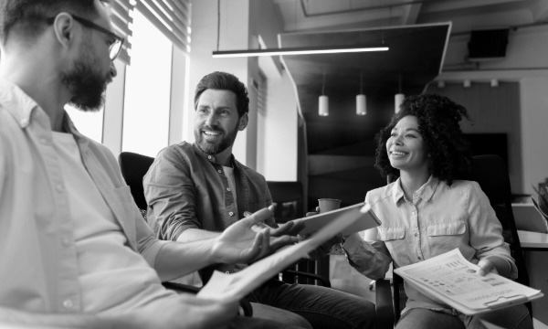 Three coworkers in an office meeting, smiling and discussing documents.