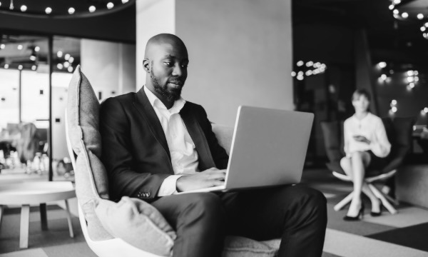 Business professional sitting in a lounge chair working on a laptop in a modern office.