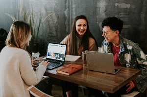 Picture of three students talking at table with laptops