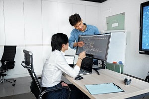 student at computer desk with teacher pointing at screen learning how to code in Python professionally