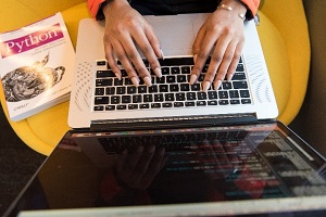 Picture of fingers on laptop next to python textbook 